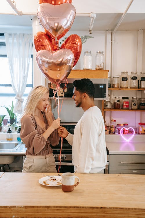 man handing a woman balloons as she smiles