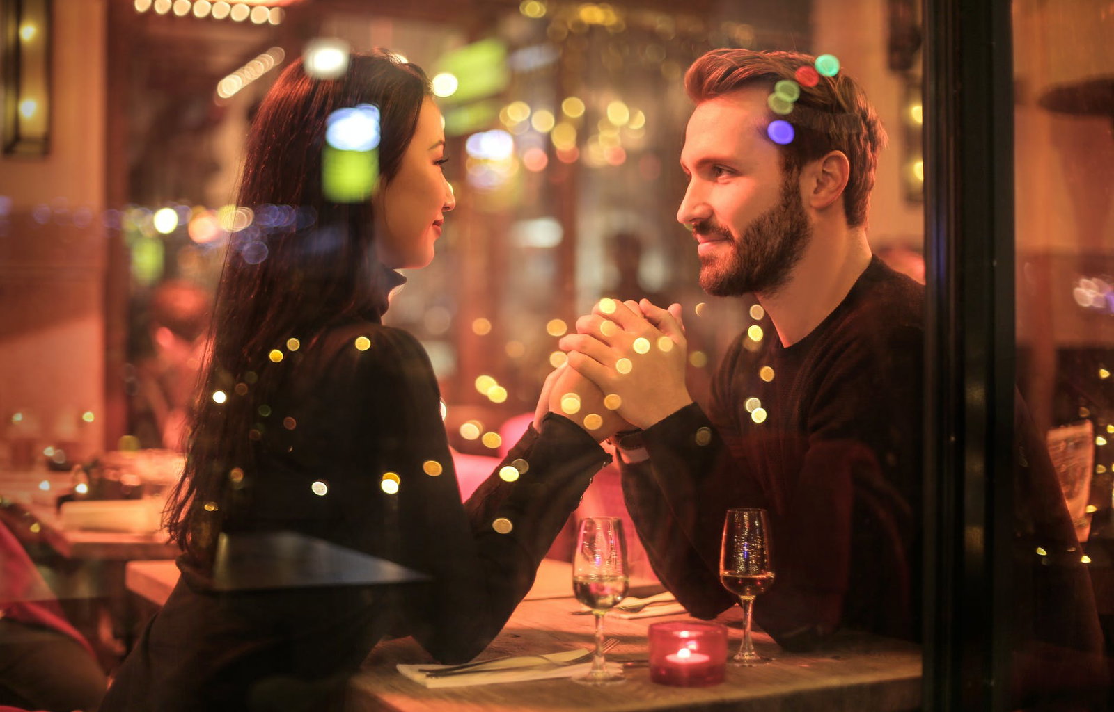 man and woman sitting at a table in a romantic restaurant as they hold hands and gaze into each other's eyes