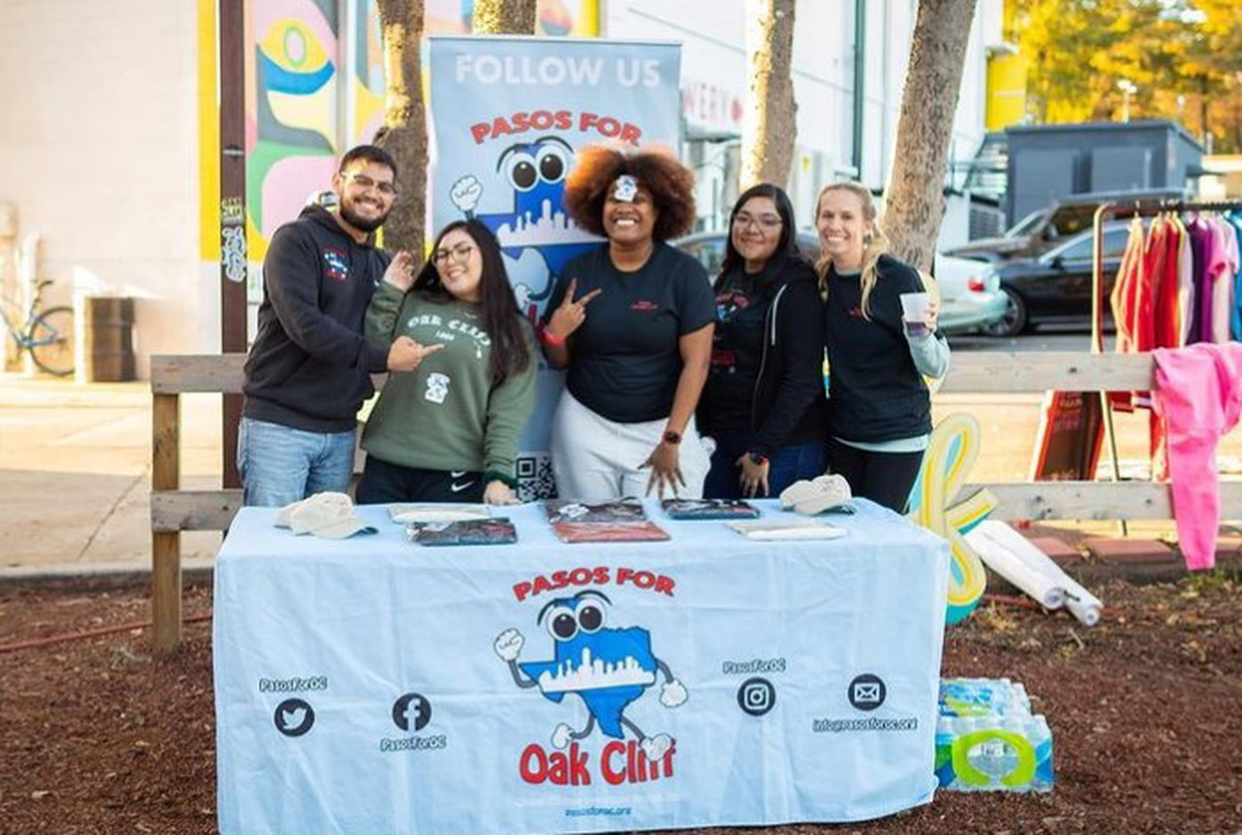 man named jesse acosta and a woman named alejandra zendejas smiling and posing with three women behind a table at a pasos for oak cliff shoe drive
