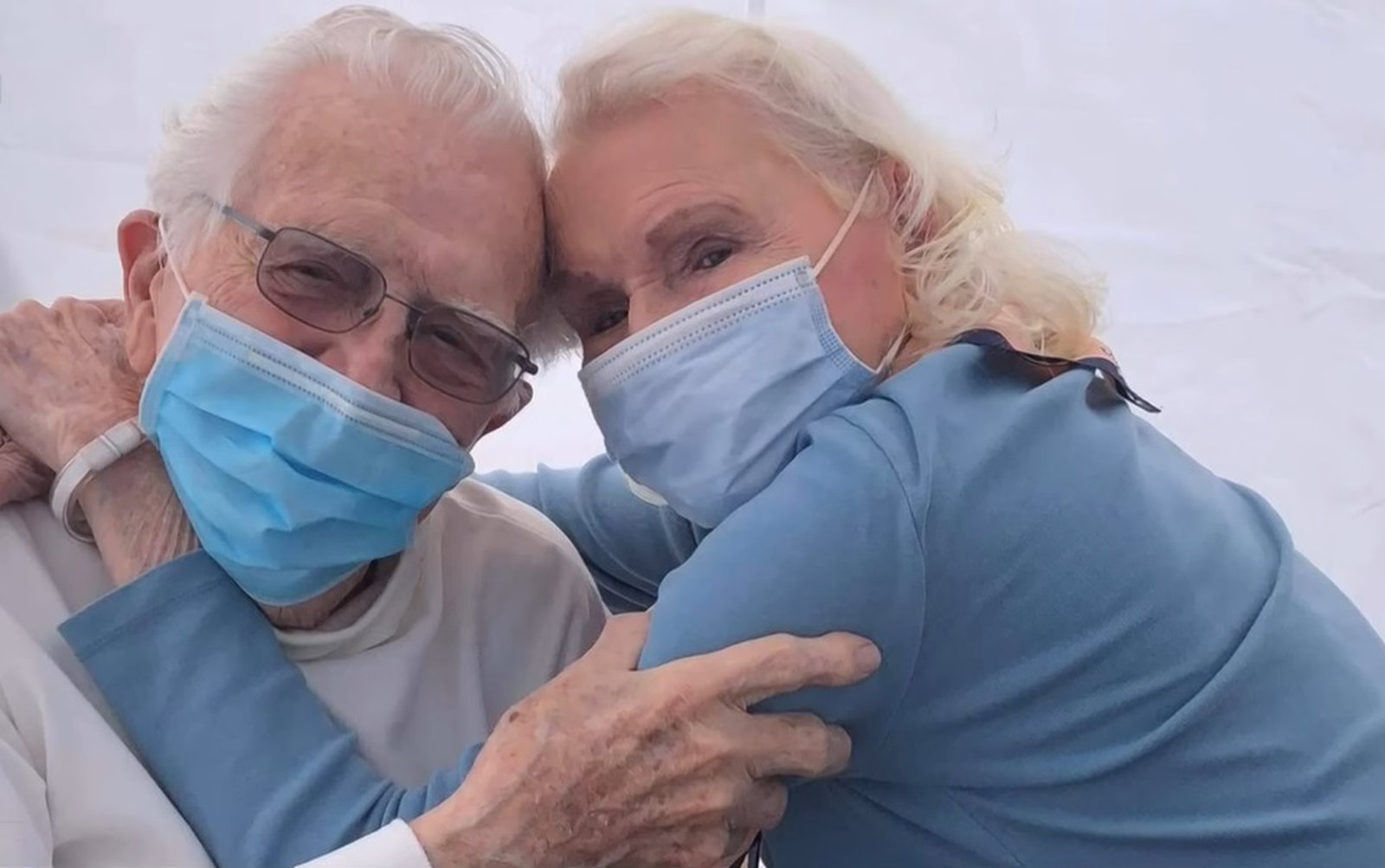 kenneth and elizabeth gage posing with their arms wrapped around each other as they each wear face masks.