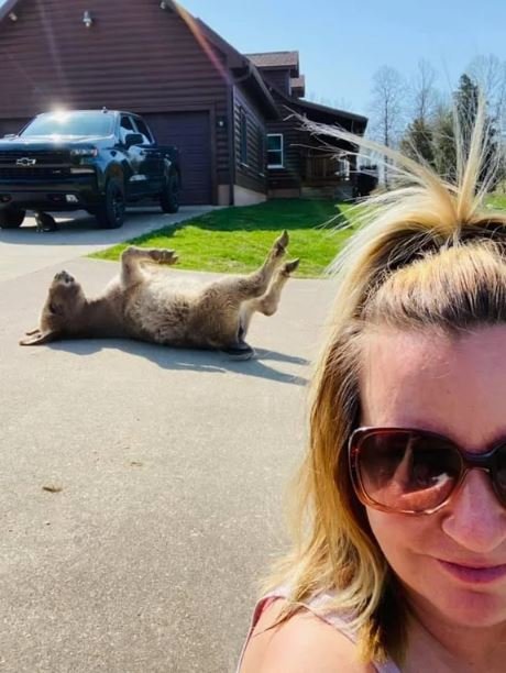 a selfie of a woman standing in front of a donkey laying on its back in the sun.