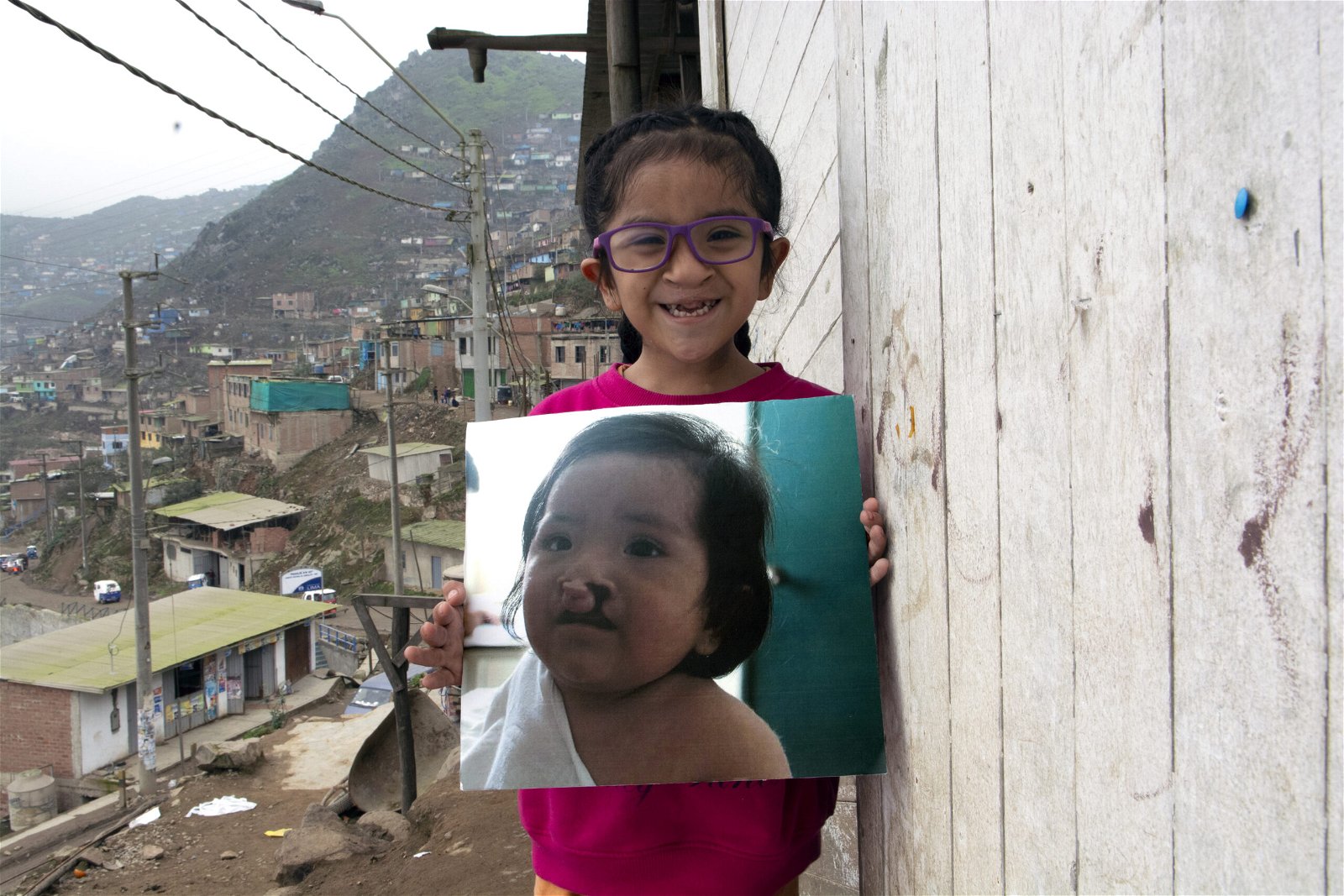 maria kristhell smiling as she stands outside and holds a photo of her as a baby.