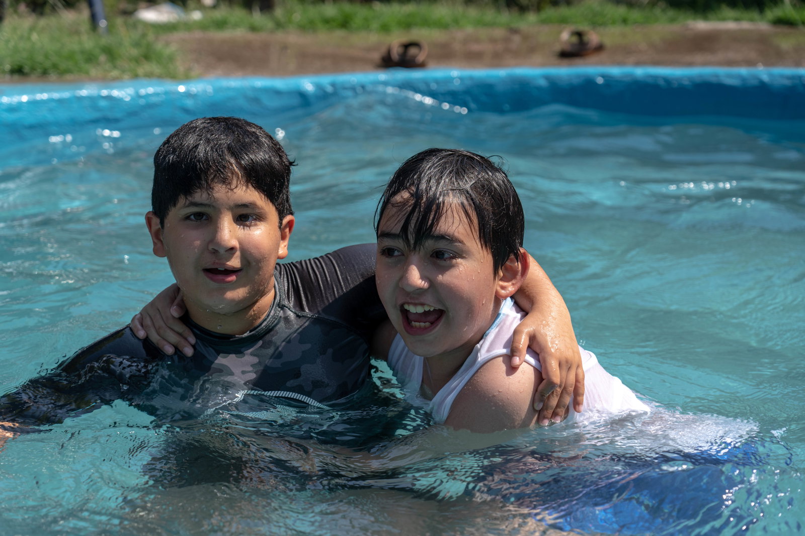 juan and another child with their arms around one another as they play in a pool.