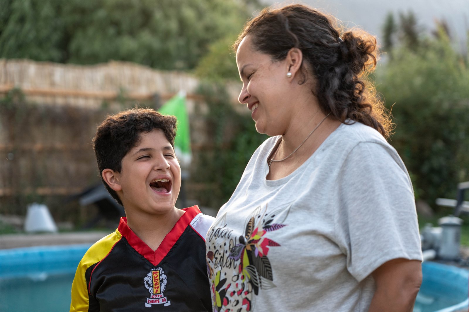 juan laughing with his mouth wide open as his mom stands with him, smiling at him.