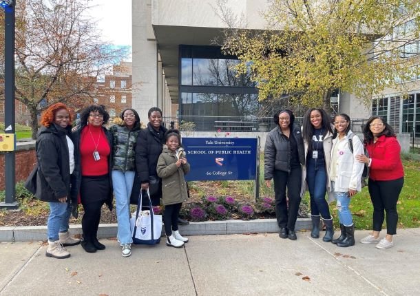A group of African-American female scientists stand near a sign on Yale University's campus, including Bobbi.