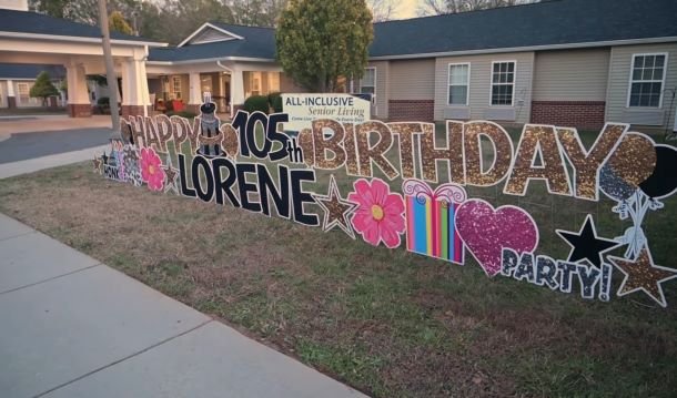A large birthday sign sits in a yard.