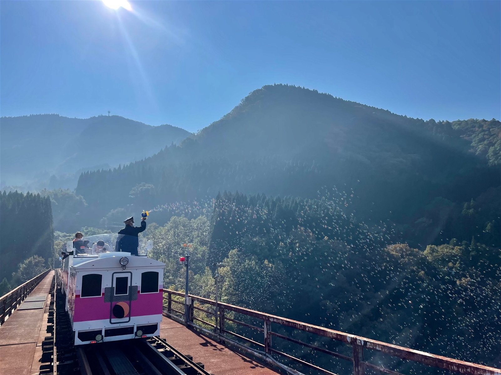 Conductor blows bubbles on Amaterasu Railway in Japan. Giant, beautiful mountains are in the distance.
